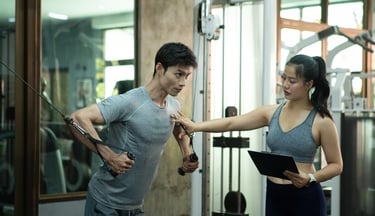A man performs cable chest fly exercises with guidance from a professional fitness trainer in a gym.