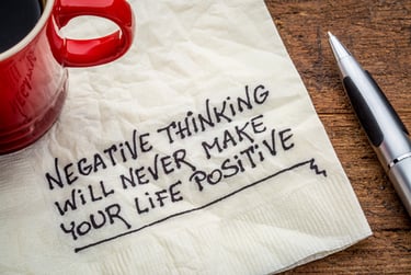 Inspirational quote on a napkin about positive thinking next to a red coffee mug and pen.