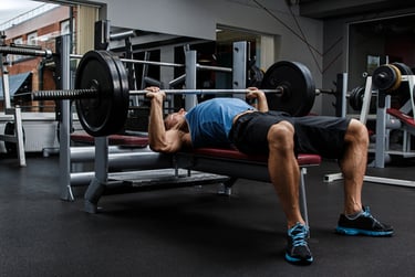 Muscular man performing a barbell bench press exercise for chest strength training in a gym.