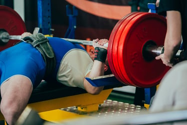 A powerlifter performing a heavy bench press with red weight plates and a lifting belt.