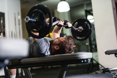 A man performing a triceps extension with a weighted barbell on a weight bench at the gym.