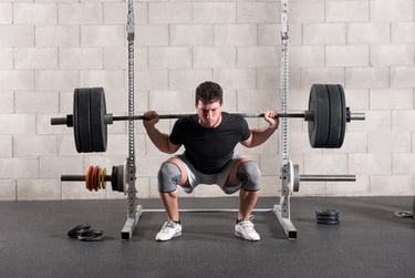 A man performing a heavy barbell back squat in a power rack at a home gym with knee sleeves.