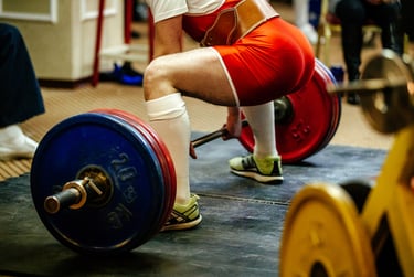 A powerlifter in red singlet performs a heavy barbell deadlift during a weightlifting competition.