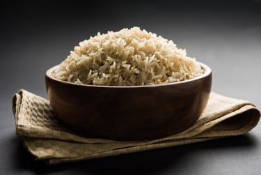 A wooden bowl filled with cooked brown basmati rice on a dark background.