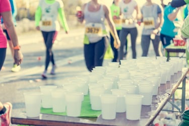Rows of water cups at a marathon hydration station for runners on a sunny race course.