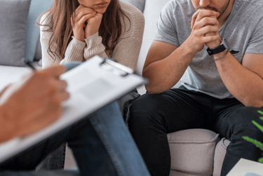 2 people, partially visible, sitting on a couch across from someone taking notes on a clipboard