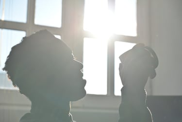 Silhouette of a person drinking coffee in front of a bright window with morning sunlight.