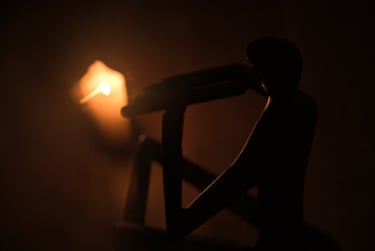Silhouette of a seated person figurine next to a glowing candle in a dark room.
