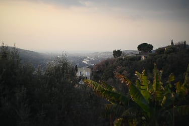 Panoramic view of a hillside village in Nice, France, overlooking a river valley at sunset.