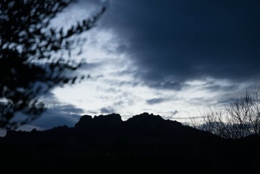 Dark silhouette of mountain peaks against a cloudy blue twilight sky at dusk.
