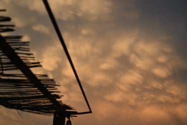 Golden mammatus clouds at sunset viewed from beneath a rustic bamboo roof structure.