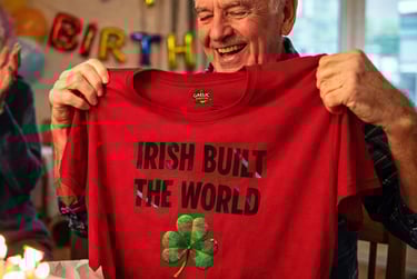 A happy senior man opening a red Irish pride t-shirt gift at a birthday celebration with balloons.