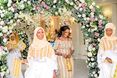 Somalian bride & bridesmaids all dressed in traditional white & cream outfits dancing and laughing , floral arch framing them