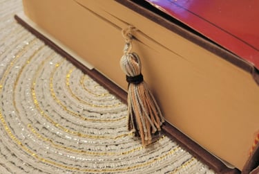 A thick hardcover book with a decorative tassel bookmark resting on a textured circular placemat.