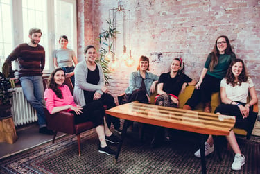 Ein Teamfoto mit einem Couchtisch vor einer Backsteinwand.