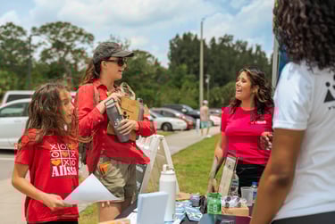 A lady wearing a red shirt with a little girl visiting an information booth