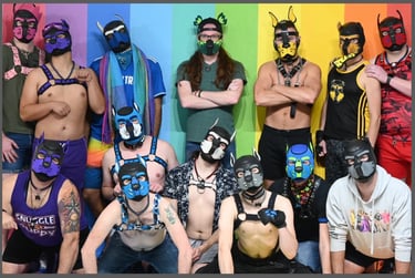 A group of men in pup masks pose together in front of a rainbow painted wall.