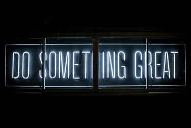 A neon sign with white lettering that reads "DO SOMETHING GREAT" is illuminated against black color
