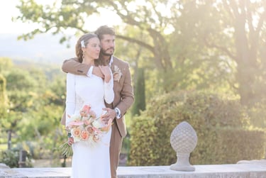 Elegant bride in a long-sleeve wedding dress and birdcage veil posing with the groom in a tan suit at a garden wedding.