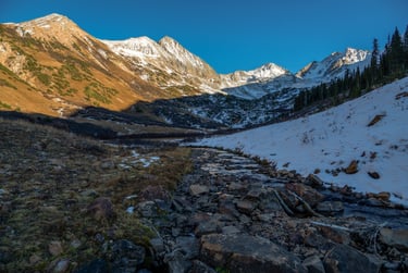 Beautiful snow-dressed high mountain peaks shine above Rustlers Gulch during fall sunset