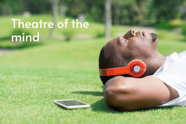 Person lying on grass with eyes closed listening to audio books sound design through headphones