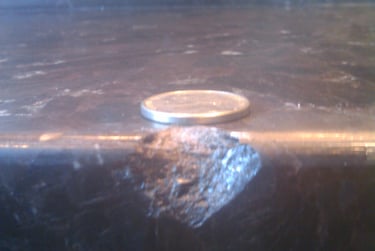 A small chip on the edge of a dark marble countertop next to a silver coin for scale.