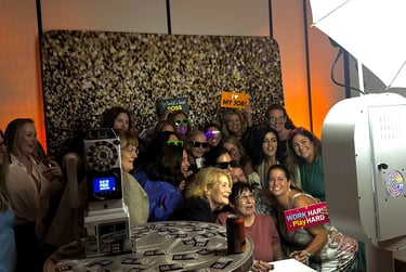 A group of coworkers enjoy a corporate event photo booth with props and a gold glitter backdrop.