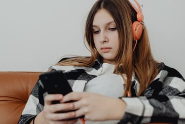 Teenage girl relaxing on a couch looking at her phone, appearing thoughtful and low-energy.