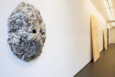 Contemporary silver textured wall sculpture displayed in a minimalist modern art gallery hallway.