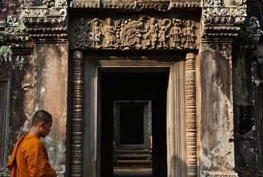 Intimate close-up of a Cambodian temple doorway at dawn, stone carvings in soft raking morning light, a monk's saffron robe partially visible at the left edge, no tourists, no flash