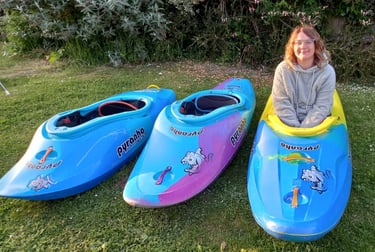 a woman sitting on a lawn with three kayaks