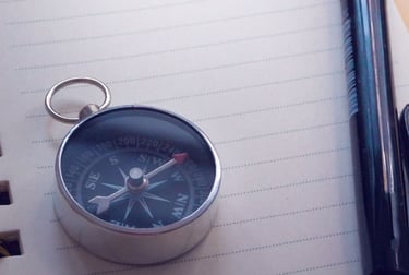 Image of compass on top of a notebook, with a pen