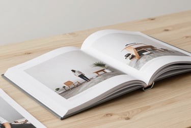High-quality photography prints and an open portfolio book on a clean wooden table in a Central European / German creative studio, soft off-white lighting, minimal aesthetic.