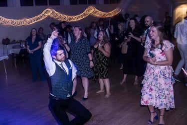 Wedding guests dancing on a wooden dance floor under festive string lights during a lively reception party.