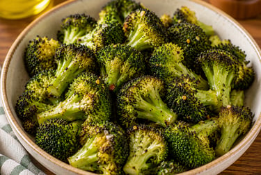 A bowl of seasoned roasted broccoli florets with charred edges on a wooden table.