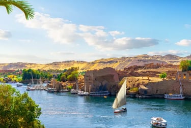 Traditional felucca sailboat and cruise boats on the Nile River in Aswan, Egypt near historic ruins.