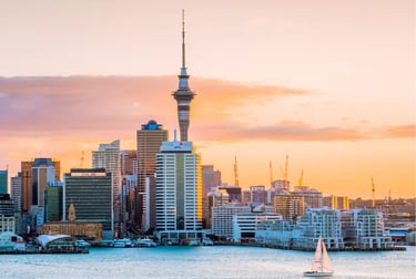 Auckland skyline and Sky Tower at sunset with a sailboat on Waitemata Harbour.