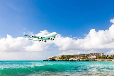 A large passenger airplane landing over the turquoise ocean and beach at Maho Beach in Saint Maarten.