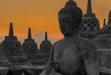 Stone Buddha statue and bell-shaped stupas at Borobudur Temple during a golden sunset in Indonesia.