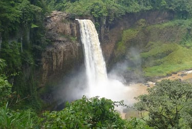 A powerful tropical waterfall cascading down a rocky cliff into a misty pool surrounded by lush green jungle.