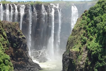 Panoramic view of Victoria Falls cascading into a rocky gorge surrounded by lush green cliffs.