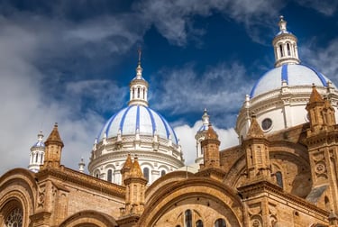 The blue and white tiled domes of the New Cathedral in Cuenca, Ecuador against a cloudy sky.