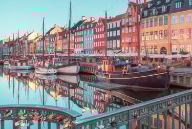 Colorful historic buildings and wooden boats in Nyhavn canal, Copenhagen, reflecting in the water.