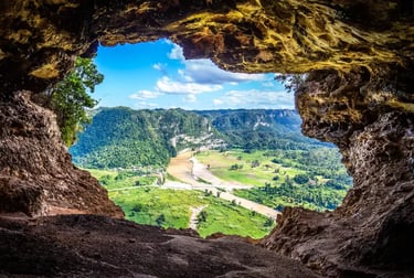 Panoramic view of a tropical river valley and green mountains seen from inside a dark rock cave.