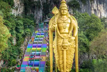 Golden Lord Murugan statue standing before the colorful rainbow stairs at Batu Caves in Malaysia.