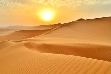 Golden sunset over rolling orange sand dunes in the vast desert landscape.