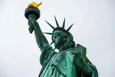 A low-angle view of the Statue of Liberty holding a golden torch against a gray sky in New York.