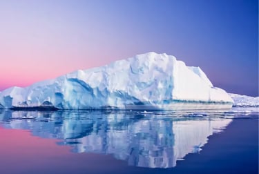 Large white iceberg reflecting in calm Antarctica waters during a pink and blue sunset.