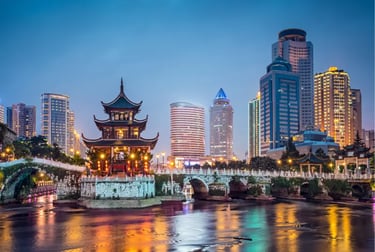 The Jiaxiu Pavilion and arched bridge at dusk in Guiyang, China with a modern city skyline backdrop.