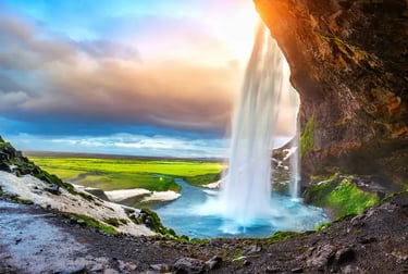 Seljalandsfoss waterfall in Iceland at sunset with golden light hitting the water and green landscape.